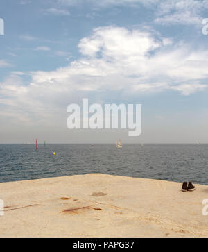 Vieille paire de chaussures de hipster minable à Seacoast brise-lames. Les petits bateaux naviguant sur la mer Méditerranée, près de la plage de Barceloneta à Barcelone, Espagne. Banque D'Images