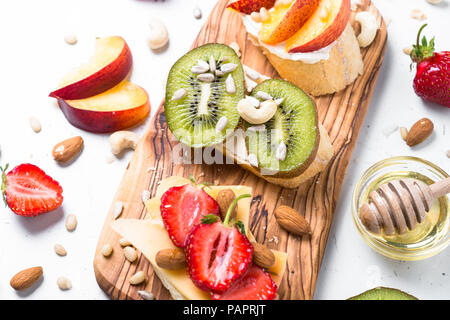 Fresh fruit sucré des sandwichs. Kiwi Fraise Pêche et des sandwichs avec les noix et miel sur tableau blanc. Collation santé. Banque D'Images