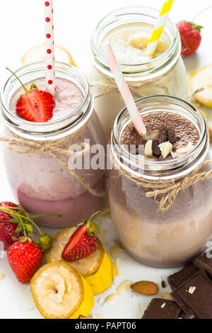 Ensemble de milkshake en pots. Banane Chocolat et Fraise milkshakes avec les écrous et la noix de coco. Dessert d'été. Alimentation saine. La verticale. Banque D'Images