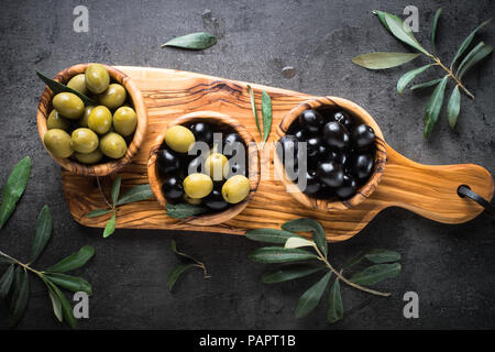 Olives noires et vertes dans bol en bois. Vue de dessus sur fond noir. Banque D'Images