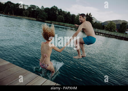 Heureux couple jumping main dans la main dans le lac de baignade Banque D'Images