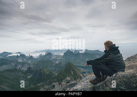 La Norvège, les îles Lofoten, Moskenesoy, jeune homme assis à Hermannsdalstinden Kjerkefjord, à plus de Banque D'Images
