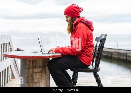 L'Islande, au nord de l'Islande, l'homme assis en face de la mer à l'aide d'ordinateur portable Banque D'Images