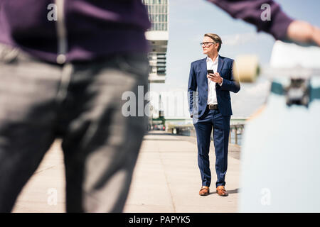 Mature businessman using cell phone et l'homme avec longboard en premier plan Banque D'Images