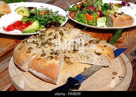 Rosemary italienne maison, vert olive et l'oignon pain focaccia sur une planche en bois avec une salade à l'arrière, Angleterre, Royaume-Uni, Europe. Banque D'Images