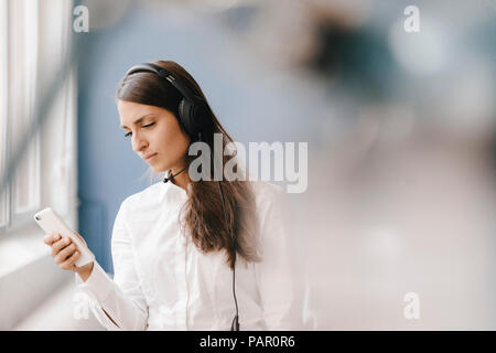 Young woman using smartphone, wearing headset Banque D'Images