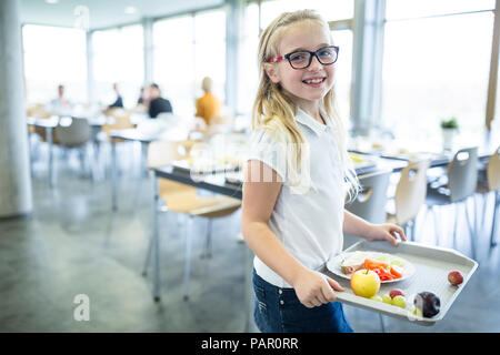 Portrait of smiling schoolgirl carrying tray en cantine scolaire Banque D'Images