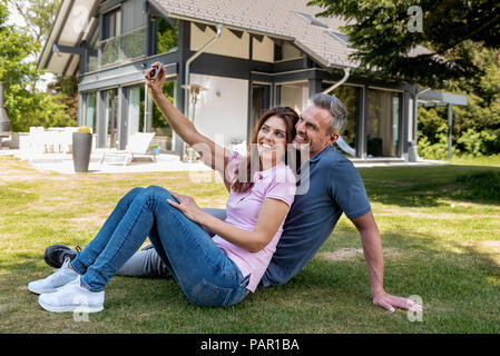 Heureux couple assis dans le jardin de leur maison en prenant un selfies Banque D'Images