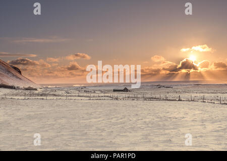 Le soleil éclate d'un nuage sur le paysage gelé de l'Islande dans l'après-midi. Les vagues de l'Atlantique Nord peut être vu s'écraser sur la plage Banque D'Images