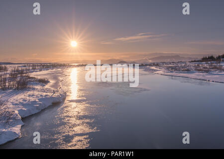 Le faible soleil réfléchi sur les eaux glacées du lac Thingvallavatn dans le Parc National de Thingvellir, Islande. Banque D'Images