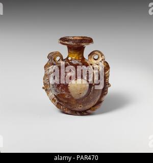 Lentoid verre aryballos (flacon de parfum). Culture : le grec. Dimensions : H.:1 15/16 in. (5 cm) ; D.:1 5/8 in. (4,2 cm). Date : 4ème-3ème siècle avant J.-C.. Brun miel translucide, avec poignées et cordon de même couleur ; les sentiers et les blobs en blanc opaque. Télévision large jante-disque avec bord arrondi et irradiant les marques des outils sur la surface supérieure ; cou cylindrique mince, effilé vers le bas ; oblique ; lentoid ; corps globulaire fond convexe ; deux grandes poignées anneau vertical attaché à l'épaule. Un sentier attaché à bord de jante-disque ; une circulaire marvered blob appliqué sur les deux faces des corps ; un grand cordon, bien positionné en couverture torsadée Banque D'Images