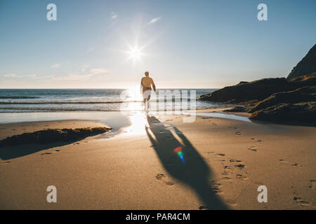 La Norvège, les îles Lofoten, Moskenesoy, homme qui marche dans le soleil à Kvalvika Beach Banque D'Images