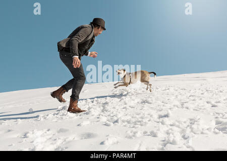 Man Playing with dog in winter, throwing snow Banque D'Images