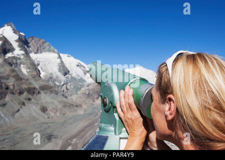 L'Autriche, la Carinthie, femme regardant à travers des jumelles pointant à pic Grossglockner et glacier Pasterze, vue de Kaiser-Franz-Josefs-Hoehe Banque D'Images