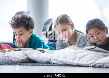 Les élèves se trouvant sur le plancher des livres de lecture à l'école de la salle de pause Banque D'Images