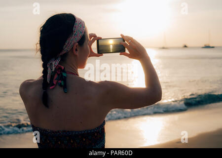 La Thaïlande, Koh Lanta, femme sur la plage photo prise avec téléphone cellulaire au coucher du soleil Banque D'Images