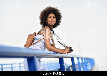 Portrait de jeune femme à la mode avec sac à dos et appareil photo debout sur un pont Banque D'Images