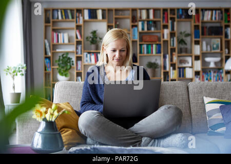 Woman at home sitting on couch using laptop Banque D'Images