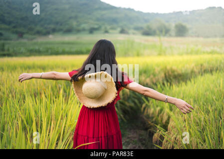 Fille qui marche dans un champ de riz wearing red dress holding un chapeau Banque D'Images