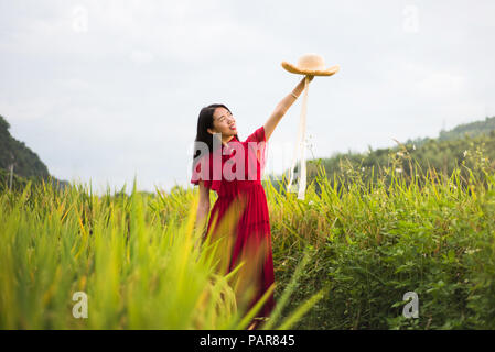 Jeune fille dans un champ de riz portant robe rouge et un chapeau Banque D'Images