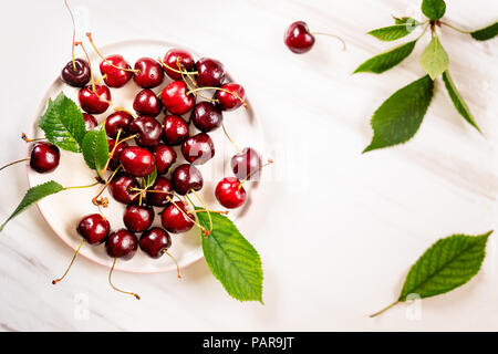 Vue de dessus de cerises sur une plaque de marbre blanc sur le fond avec des feuilles vertes Banque D'Images