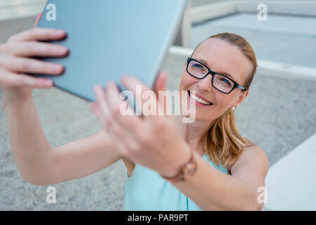 Portrait of smiling woman wearing glasses en tenant avec selfies tablet Banque D'Images
