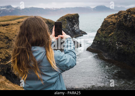 Vue arrière de l'Islande, young woman taking picture with smartphone at coast Banque D'Images