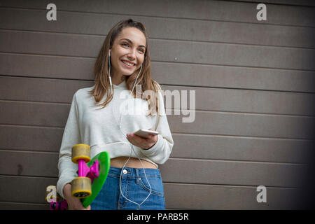 Smiling woman with cell phone, écouteurs et skateboard Banque D'Images