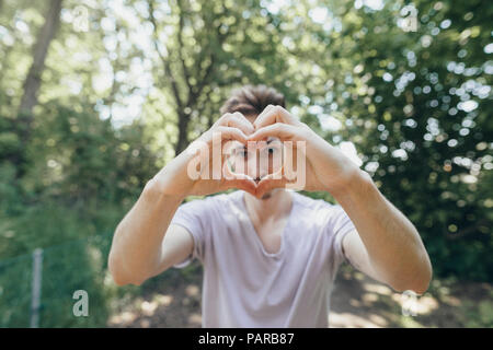 Jeune homme faisant un coeur avec ses doigts sur le chemin forestier Banque D'Images