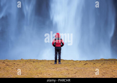 Cascade de Seljalandsfoss en Islande. Guy en veste rouge ressemble à une cascade de Seljalandsfoss. Banque D'Images