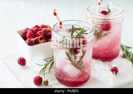 Les boissons gazeuses. Boisson d'été rafraîchissante framboise avec le romarin et la glace. Verres à eau froide et de boissons sains sur une table de cuisine en bois. Banque D'Images