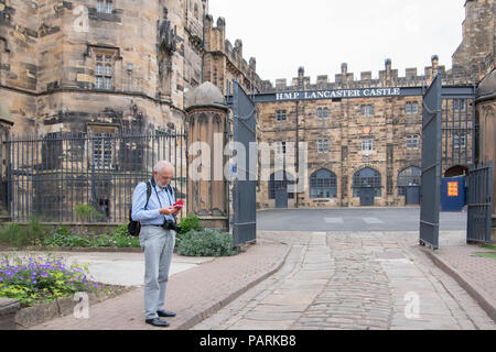 Un homme âgé avec sac à dos à la recherche de téléphone mobile avec la prison de Lancaster et le château derrière montrant la cour et HMP sign Banque D'Images