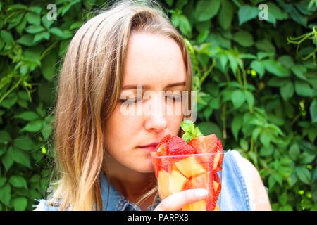 La fille est heureuse de respirer l'arôme de fruits frais qui sont coupés en morceaux et mettez dans un récipient. Elle ferma les yeux de plaisir et d'un h Banque D'Images