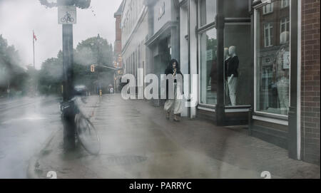 Il pleut à Stratford, une femme, décidément dans une hâte, protège la tête et marche vite, tout en jetant un regard sur une vitrine. Banque D'Images