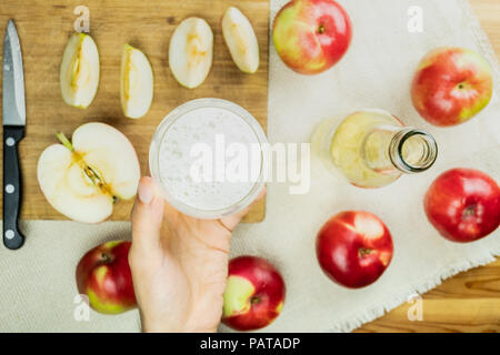 Mise à plat avec un verre de cidre mousseux verre sur table en bois rustique. Point de vue de la main qui tient le verre de cidre fait maison et biologiques cultivés localement Banque D'Images