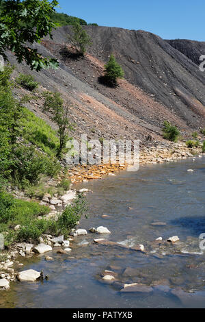 Déchets de résidus de mine de charbon le tas de déblais à côté d'un ruisseau à l'orange rochers montrant les dommages environnementaux de la pollution toxique et le drainage minier acide. Banque D'Images