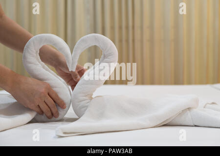 Close-up de mettre les mains de oiseaux cygnes plié les serviettes de bain blanc frais sur le drap de lit dans l'hôtel. Banque D'Images