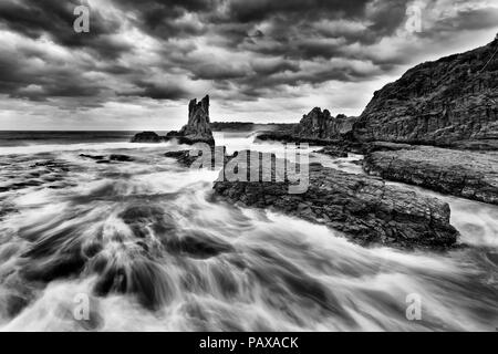 Or de grès érodé les roches de la cathédrale à Bombo plage à Kiama, NSW, Australie, au coucher du soleil orageux sous ciel nuageux en noir blanc. Banque D'Images