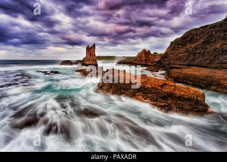 Cathédrale d'or de grès colorés des pierres sur la plage de Bombo à Kiama, NSW, Australie, au coucher du soleil orageux sous ciel nuageux. Banque D'Images