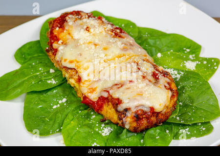 Parmesan Poulet sur un lit d'épinards avec un peu de fromage parmesan frais sur le dessus sur une plaque blanche Banque D'Images