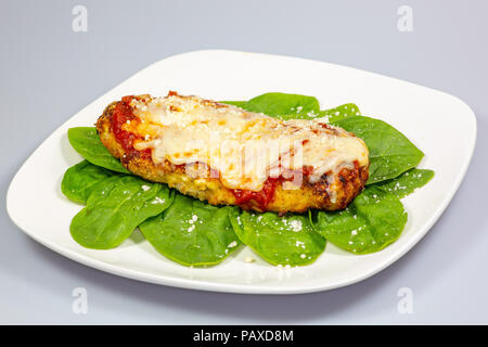 Parmesan Poulet sur un lit d'épinards avec un peu de fromage parmesan frais sur le dessus sur une plaque blanche Banque D'Images