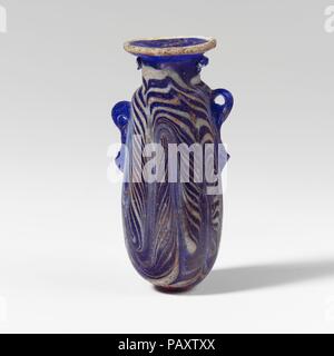Alabastron en verre (flacon de parfum). Culture : le grec, l'Est de la Méditerranée. Dimensions : H. : 2 1/2 in. (6,4 cm). Date : fin 6ème-5ème siècle avant J.-C.. Bleu cobalt translucide, avec poignées de même couleur ; sentiers en blanc opaque. Rim horizontale légèrement concave-disque, de la projection de l'bord rugueux à la bouche ; cou cylindrique arrondi étroit ; l'épaule ; côtés légèrement convexe à corps cylindrique, effilé vers le haut ; bas convexe ; deux poignées anneau vertical avec queues bulbés, appliquée sur un sentier décoration ; plus grande et plus haute que l'autre. Un sentier attaché à bord de jante-disque ; un autre sentier appliqué sur le cou Banque D'Images