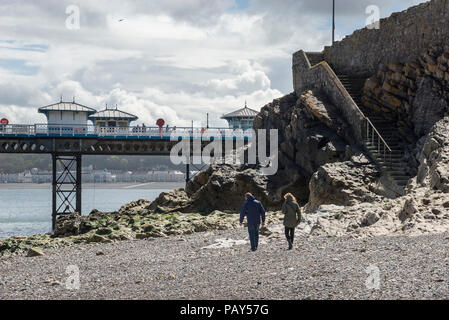 Couple en train de marcher sur la plage rocheuse ci-dessous jetée de Llandudno, sur la côte du nord du Pays de Galles, Royaume-Uni. Banque D'Images