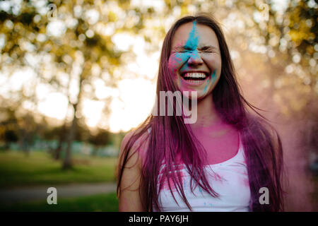 Portrait of a smiling young woman with face enduite de couleurs. Cheerful girl au parc avec poudre de couleur sur son visage. Banque D'Images