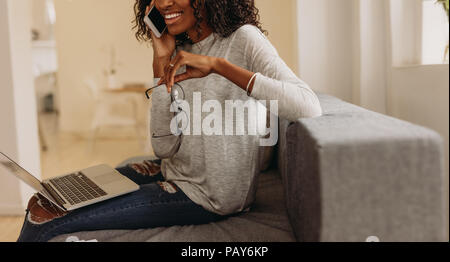 Femme entrepreneur mode dans le jean déchiré parlant au téléphone mobile avec un ordinateur portable sur ses genoux. Businesswoman sitting on sofa at home parler o Banque D'Images