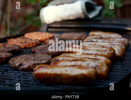 Rangées de saucisses cuites et hamburgers sur un barbecue Banque D'Images