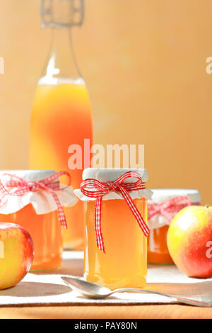 Jus de pommes maison dans une bouteille en verre et la gelée dans les pots avec lin et un nostalgique ribbon bow en plein soleil devant un fond de couleur abricot. Banque D'Images