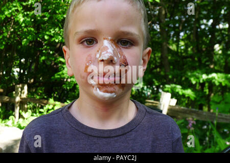 Un jeune garçon (6 ans) à visage couvert dans le chocolat après avoir mangé une glace Banque D'Images