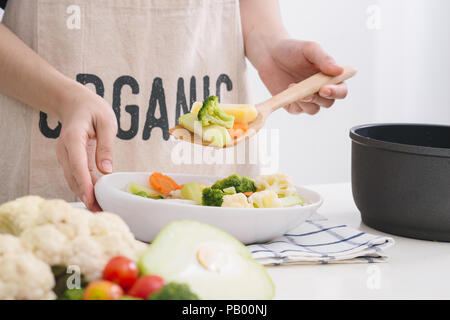 Femme dans la cuisine cuisine légumes sautés à la poêle et dégustation. Banque D'Images