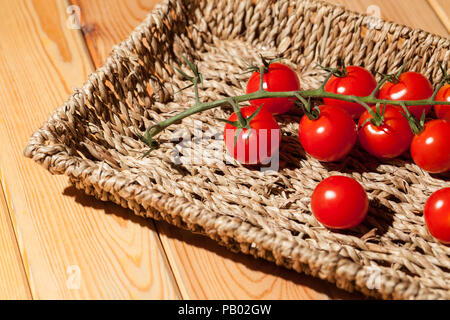 Vigne rouge cerise tomates mûries au soleil piccolo dans panier en osier rouge sucré sain bac tomate miniature organique tige. Banque D'Images
